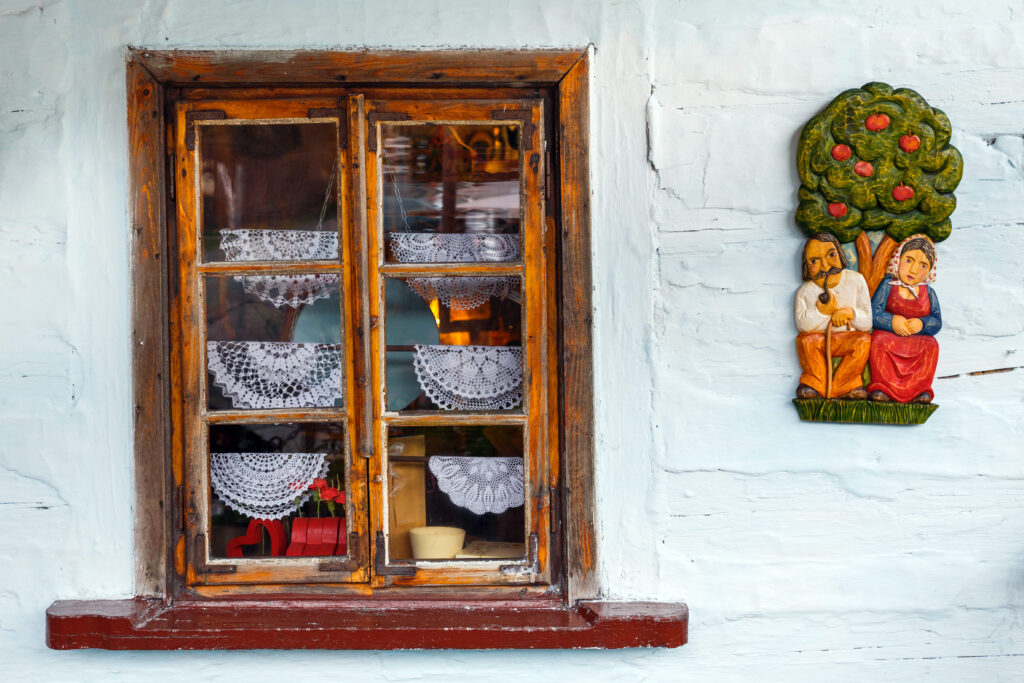 Drewniane okno z koronkowymi firankami i tradycyjnym wystrojem wnętrza w Lanckoronie