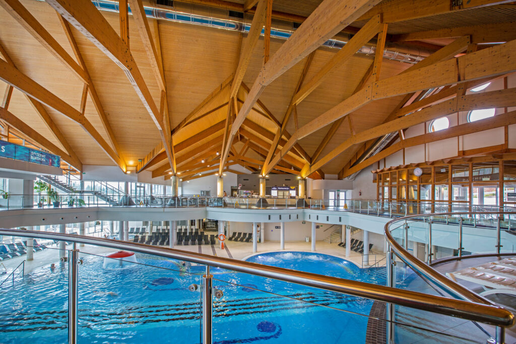 Widok z antresoli na główną halę basenową z drewnianym dachem w Aquaparku Terma Bukovina