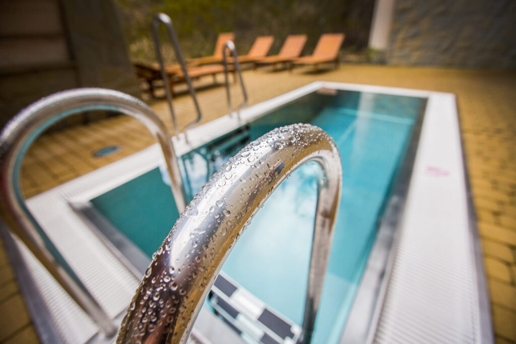Zbliżenie na stalową poręcz i basen z leżakami w tle w Aquaparku Terma Bukovina