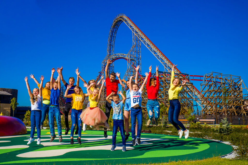 Grupa dzieci skaczących z radości na tle kolejki górskiej w Energylandii