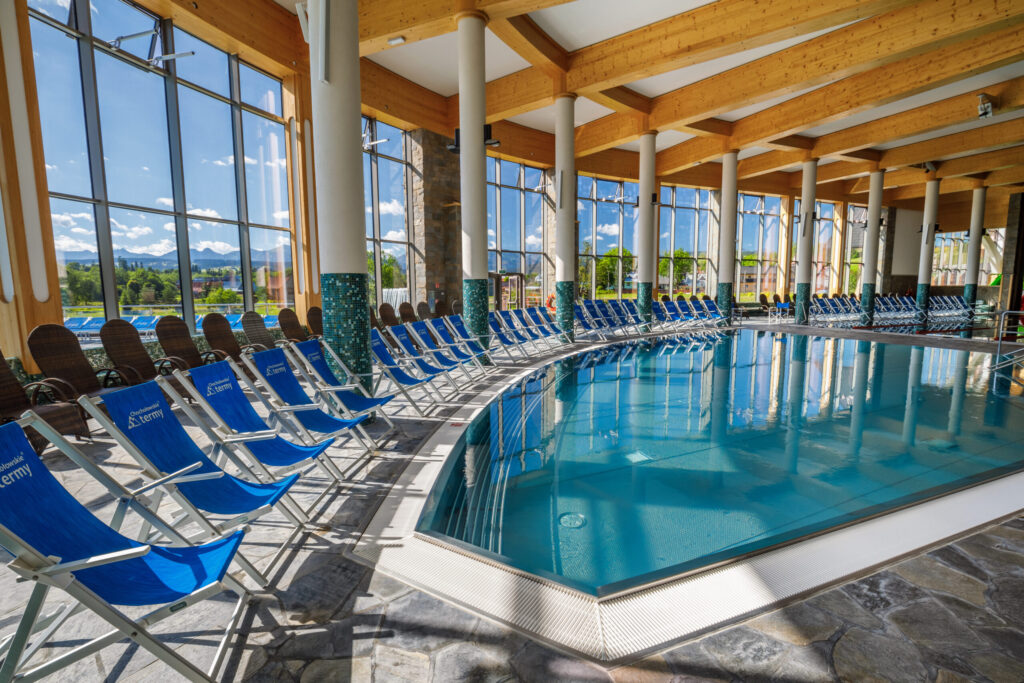 Relaksacyjna strefa basenowa z leżakami i panoramicznymi oknami w Chochołowskich Termach