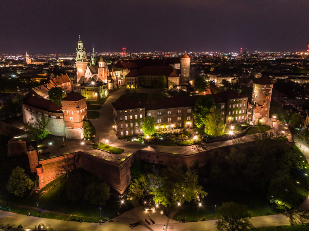 Zamek Królewski na Wawelu nocą, podświetlony, z panoramą Krakowa w tle