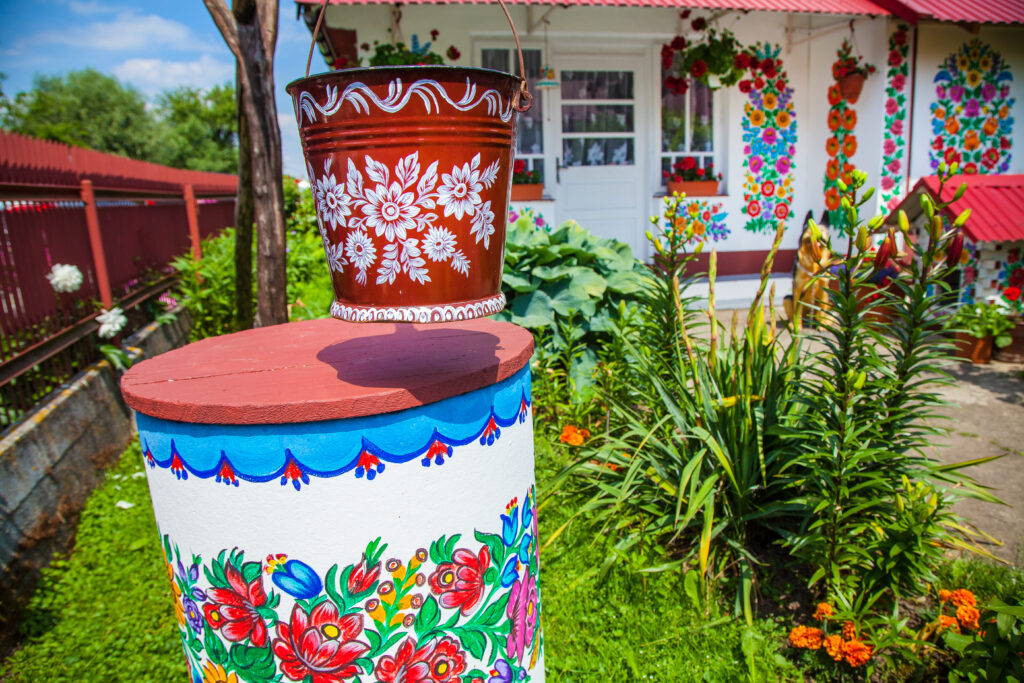 Malowana studnia z donicą i tło ozdobione wzorami kwiatowymi charakterystycznymi dla Zalipia